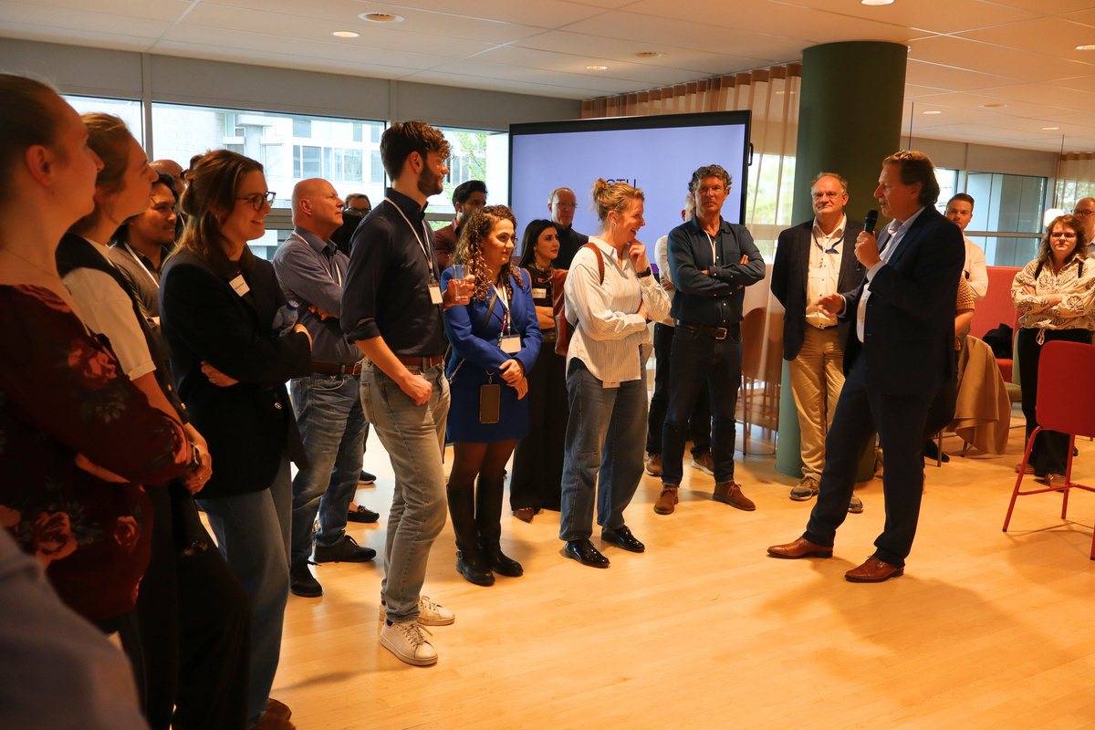 Deelnemers van de Gem Kwartaalupdate staan in een zaal bij ICTU en luisteren naar een spreker met microfoon