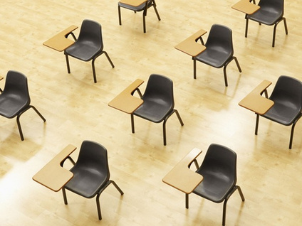 Rijen lege examenstoelen met klaptafeltjes in een zaal
